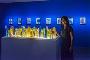 古皮特於高美館《跨越海洋》個展留影，圖中作品前為〈豐饒中的匱乏時代〉，後為〈水的殘餘〉。